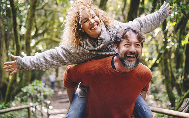 Overjoyed adult couple have fun together at outdoor park in leisure activity. Man carrying woman in piggyback and laugh a lot. Love and life mature people lifestyle concept. Enjoying vacation nature