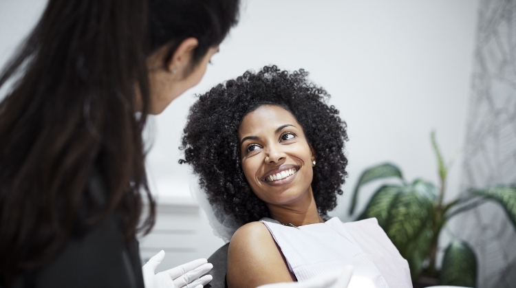 Smiling woman with curly hair at a dental clinic, interacting with a friendly dentist or healthcare professional during a checkup, in a modern medical office setting.